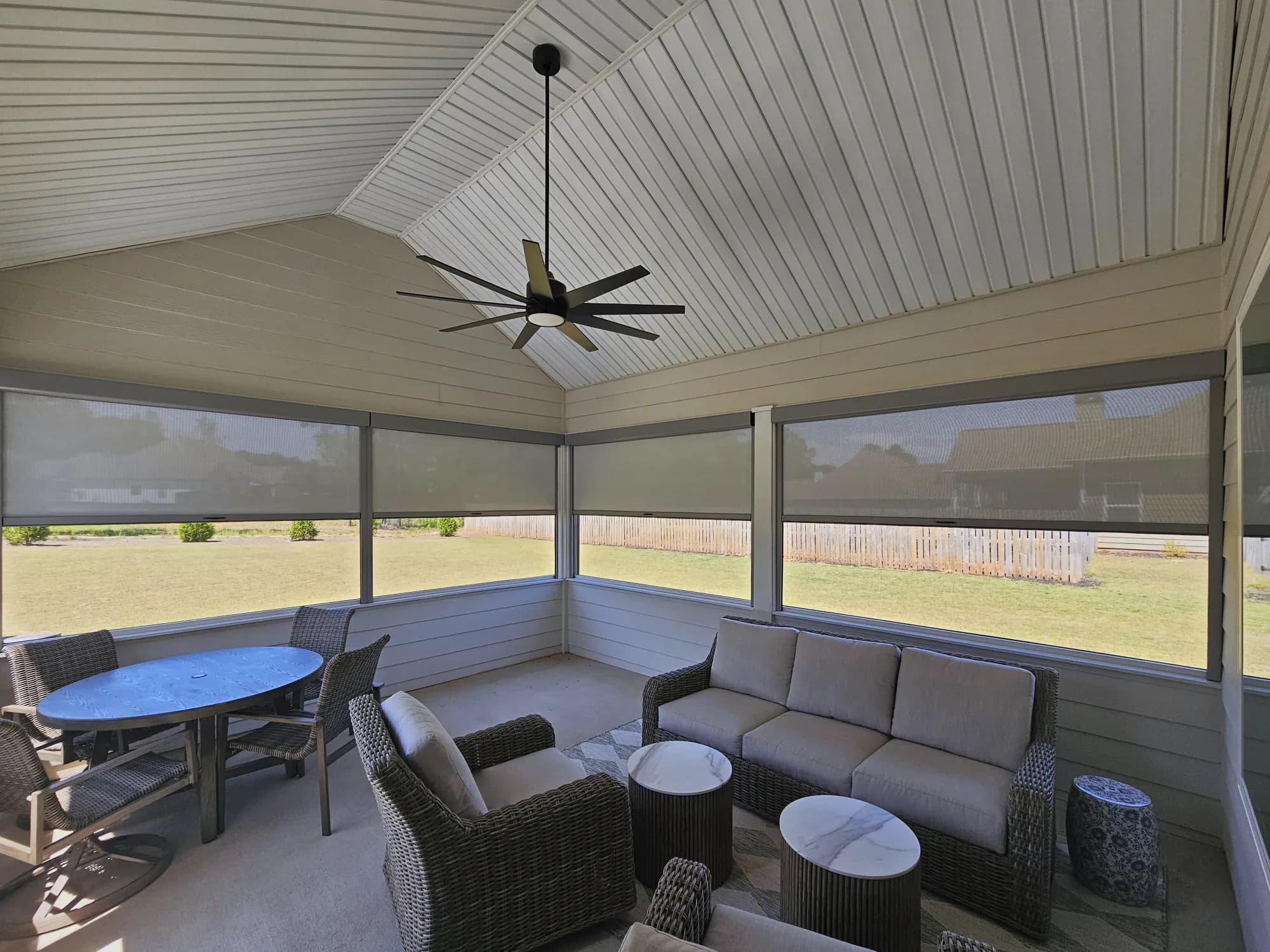 Retractable screens lowered halfway on every opening of a covered porch, with wicker seating under a vaulted ceiling.